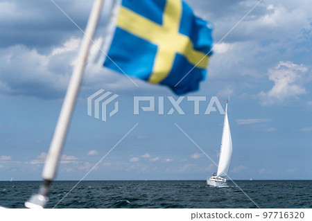 Sailboat on blue open sea with Sweden flag foreground. Concept of travel, adventure and vacation. 97716320