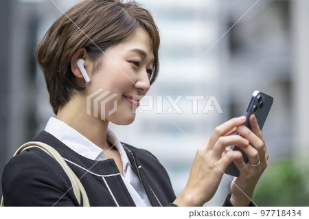 A business woman in her thirties who wears earphones and operates a smartphone 97718434