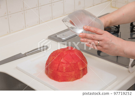 [A middle-aged housewife prepares cut watermelon, flipping the watermelon on the cutting board and transferring it to a bowl] 97719252