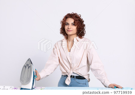 A young girl stands by the ironing board and iron. A young girl stands by the ironing board and iron. 97719939