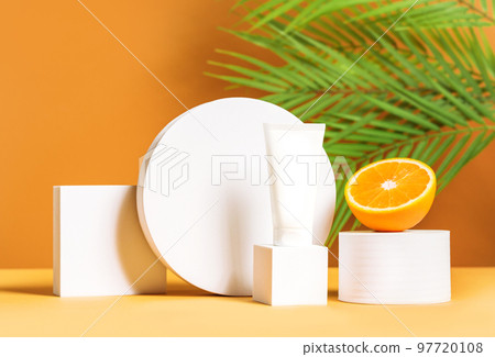Front view mock up scene with unbranded white cosmetic tube on white podium and orange on a palm leaves background. Lotion, cream, hand cream, sunscreen, moisturizer mockup. Front view mock up scene with unbranded white cosmetic tube on white podium and orange on a palm leaves background. Lotion, cream, hand cream, sunscreen, moisturizer mockup. 97720108