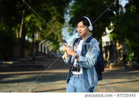 Pleasant man traveller using smart phone while walking in the city park on beautiful day. Travel, vacation and journey concept Pleasant man traveller using smart phone while walking in the city park on beautiful day. Travel, vacation and journey concept 97720343