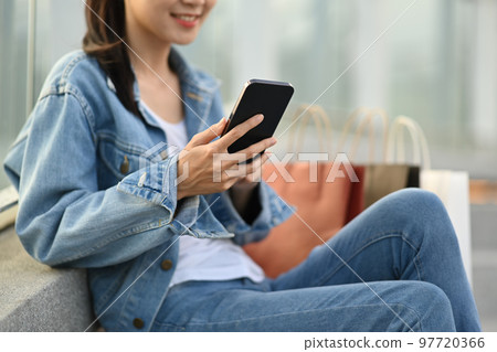 Happy woman sitting on rooftop stair with shopping bags and using smart phone. Cropped shot 97720366