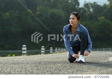 Photo of sportswoman tying shoelace before running outdoors. Fitness, sport and healthy lifestyle concept Photo of sportswoman tying shoelace before running outdoors. Fitness, sport and healthy lifestyle concept 97720390