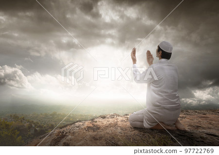 Rear view of a Muslim man sitting while raised hands and praying 97722769