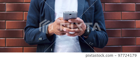 Leisure time. Young guy standing leaning on wall browsing internet on smartphone smiling cheerful close-up 97724179
