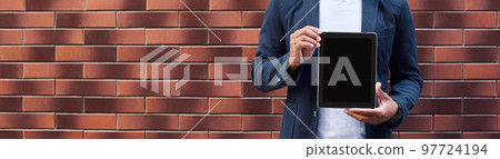 Promotion. Young guy standing on wall showing screen of digital tablet looking camera smiling happy 97724194