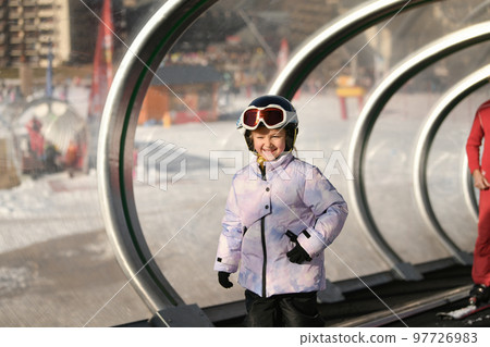 A girl on skis stands on a carpet ski lift in a glass tunel 97726983