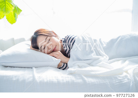 A woman sleeping on a bed in a bright simple room 97727126