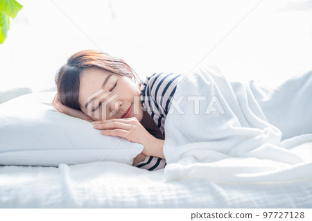 在一間明亮的簡單房間裡睡在床上的女人 97727128