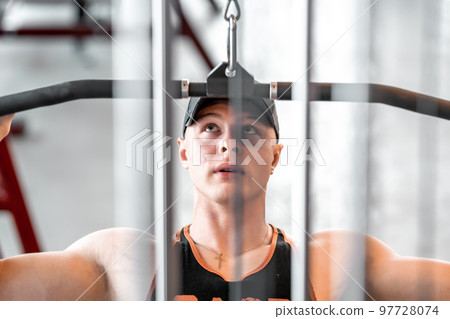 exercise of the back muscles by pulling the pulley on the strength machine exercise of the back muscles by pulling the pulley on the strength machine 97728074