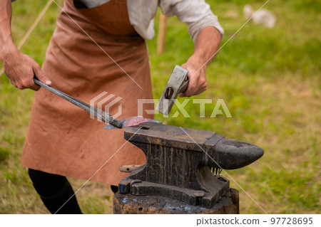 Blacksmith working with metal on anvil at outdoor workshop - close up Blacksmith working with metal on anvil at outdoor workshop - close up 97728695