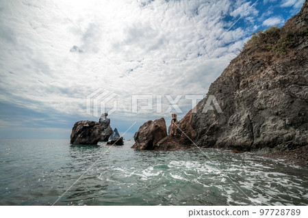 Woman swimsuit sea. Attractive blonde woman in a black swimsuit enjoying the sea air on the seashore around the rocks. Travel and vacation concept. 97728789