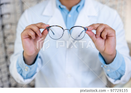 Man in a lab coat holding eyeglasses in hands 97729135