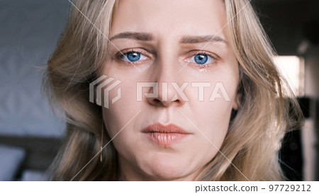 Portrait of crying grieving woman of 30 years. Grimace of sadness with tears in her eyes and crooked chin of blonde woman looking at camera. Emotional swing, unstable psyche, mental problems 97729212