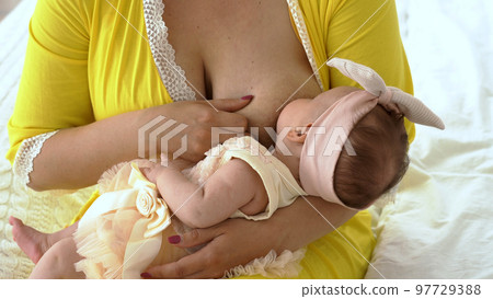 Young woman breastfeeding her baby while sitting on bed 97729388