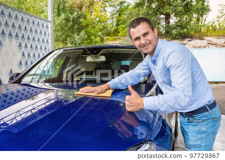 Man polishing car on a car wash. The man holds the microfiber in hand and polishes the car Man polishing car on a car wash. The man holds the microfiber in hand and polishes the car 97729867