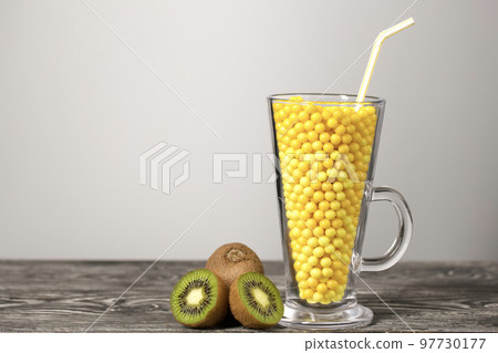 The glass goblet is filled with vitamins in the form of dragees. Kiwi halves nearby. On black pine boards. On a white background. 97730177