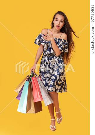 Fashion portrait young woman wearing a shopping bags, straw hat, dress posing over colorful yellow background 97730655