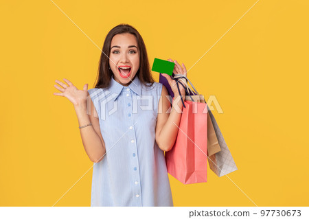 Charming pretty attractive sexy girl showing credit card and holding many colorful packages in hand, it is comfortable to use bank card for shopping, standing over yellow background Charming pretty attractive sexy girl showing credit card and holding many colorful packages in hand, it is comfortable to use bank card for shopping, standing over yellow background 97730673