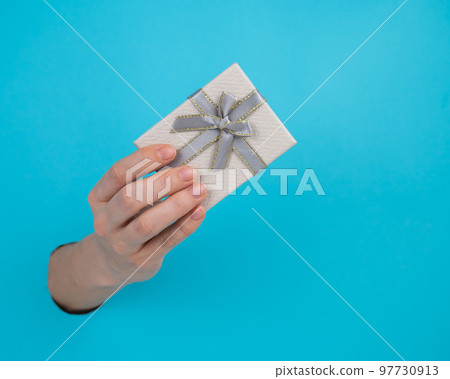 A woman's hand sticks out of a blue paper background and a gift box. A woman's hand sticks out of a blue paper background and a gift box. 97730913