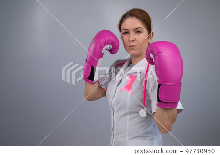 Serious female doctor in pink boxing gloves with a pink ribbon on a gray background. Fight against breast cancer.  97730930