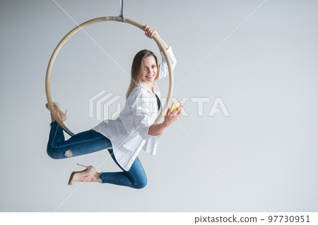 Caucasian female gymnast doing aerial hoop exercises and using smartphone.  97730951