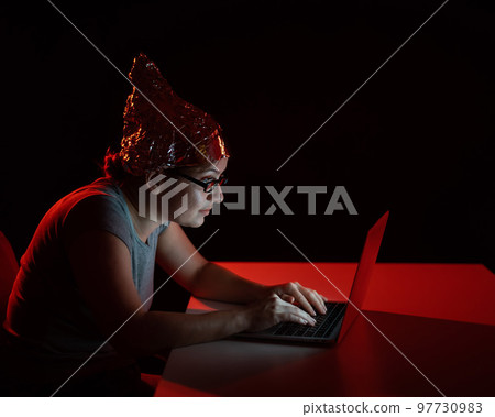 Paranoid caucasian woman typing on a computer wearing a tinfoil cap. Conspiracy theory. 97730983