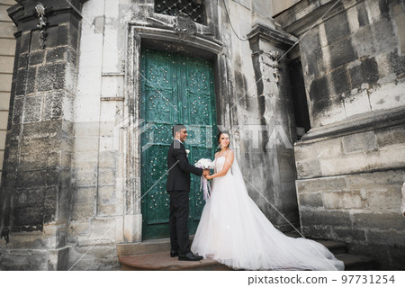 Gorgeous happy couple standing close to each other and looking in eyes at old city background, wedding photo, European city, wedding day in Lviv Gorgeous happy couple standing close to each other and looking in eyes at old city background, wedding photo, European city, wedding day in Lviv 97731254