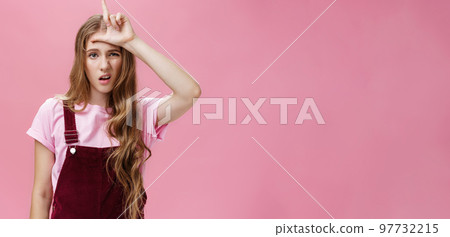 Waist-up shot of arrogant young girl with high ego grimacing snobbish showing letter L on forehead mocking over guy who lose calling person loser with scorn and disdain over pink background Waist-up shot of arrogant young girl with high ego grimacing snobbish showing letter L on forehead mocking over guy who lose calling person loser with scorn and disdain over pink background 97732215