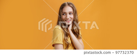 Soft and tender beautiful young girl with wavy fair hair turning back and look right touching neck gently smiling silly and sincere feeling pretty and self-assured posing over orange background Soft and tender beautiful young girl with wavy fair hair turning back and look right touching neck gently smiling silly and sincere feeling pretty and self-assured posing over orange background 97732370