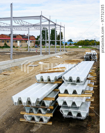 Stack of new corrugated steel roof sheets and unfinished steel framework building in background 97732385