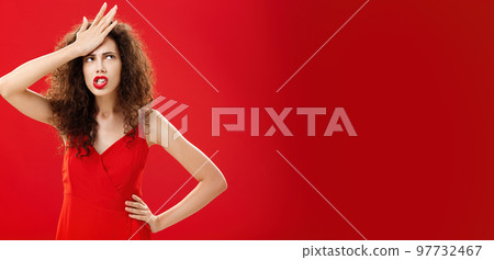 Woman feeling irritated of stupid waiter messing up order punching forehead from annoyance rolling eyes up in anger frowning, swearing saying cursing words displeased standing in red dress 97732467