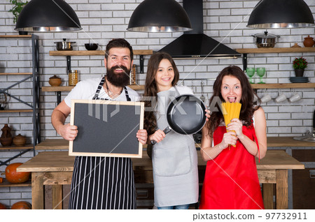 Father, mother and child cooking. Mother father with little girl. Family day. Happy family in kitchen. Little girl with parents in apron. Bearded man with board, copy space. Cooking with passion 97732911
