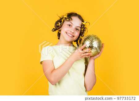 Retro party. Cheerful girl with disco ball. Fashion kid posing with curlers in hair. Fancy teen. Hairstyle for disco party. Have fun. Night club. Hairdresser salon. Child hold golden disco ball 97733172