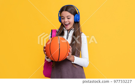 amazed kid in headphones with school backpack and basketball ball on yellow background 97733227