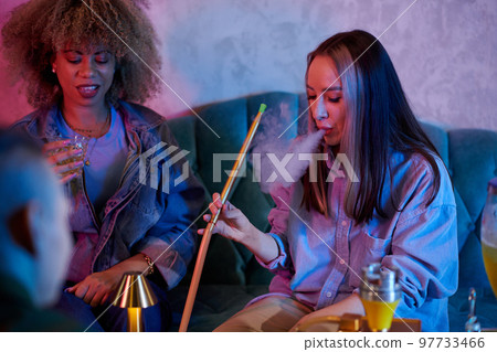 Young woman smoking hookah when spending time with friends in bar Young woman smoking hookah when spending time with friends in bar 97733466