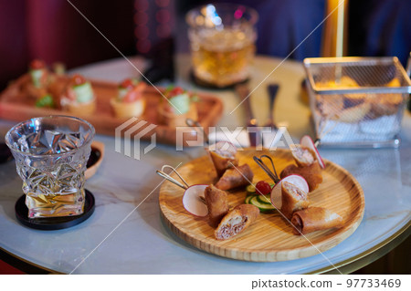 Plate with snacks and glass of alcoholic drink on table in bar or restaurant 97733469