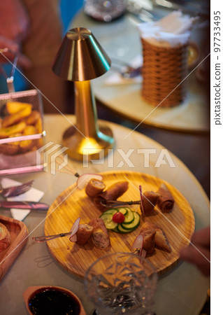 Wooden round plate with delicious snacks on cafe table Wooden round plate with delicious snacks on cafe table 97733495