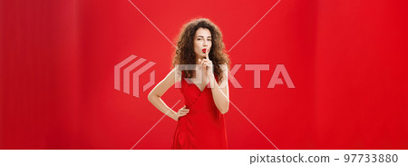 Shh let us keep it between us. Attractive and elegant adult successful woman in stylish evening dress shushing with index finger over mouth hiding secret or making surprise over red background Shh let us keep it between us. Attractive and elegant adult successful woman in stylish evening dress shushing with index finger over mouth hiding secret or making surprise over red background 97733880