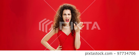 Girl chowing her temper to employees being fed up with unappropriate behaviour complaining standing pissed and dissatisfied gesturing with palm and holding hand on hip over red background 97734706