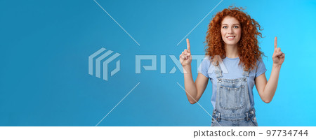 Motivated happy cheerful redhead silly curly woman pointing up inrdex finger smiling charmed impressed excited showing awesome promo discuss interesting advertisement blue background Motivated happy cheerful redhead silly curly woman pointing up inrdex finger smiling charmed impressed excited showing awesome promo discuss interesting advertisement blue background 97734744