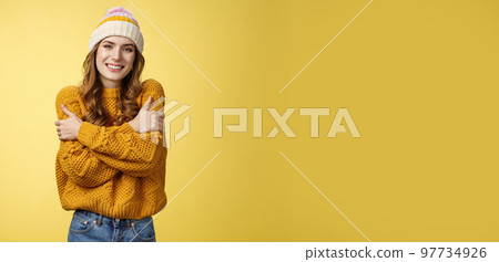 Getting cold bring jacket. Portrait charming tender feminine cute girlfriend embacing herself cuddling smiling warm gaze freezing outside standing knitted sweater hat, yellow background 97734926