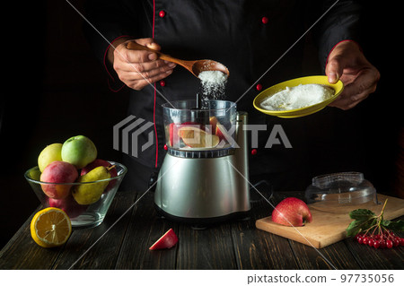 The chef cooks a refreshing drink from fresh fruits in an electric blender. The cook adds sugar to the mixer with a spoon. Menu idea for a hotel or restaurant. The chef cooks a refreshing drink from fresh fruits in an electric blender. The cook adds sugar to the mixer with a spoon. Menu idea for a hotel or restaurant. 97735056