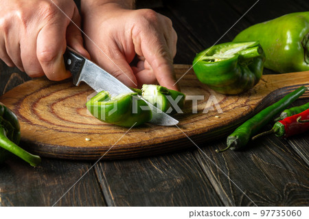 Slicing green fresh peppers on a cutting board by the hands of a cook to prepare a delicious lecho at home. Slicing green fresh peppers on a cutting board by the hands of a cook to prepare a delicious lecho at home. 97735060