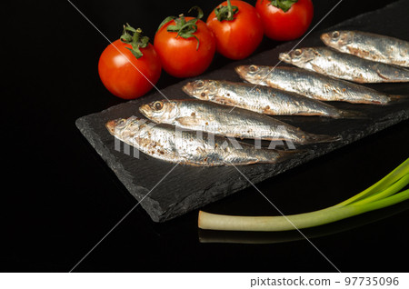 Sprat with vegetables on a serving black board. Small salted fish with onions and tomatoes. Delicious breakfast ideas Sprat with vegetables on a serving black board. Small salted fish with onions and tomatoes. Delicious breakfast ideas 97735096