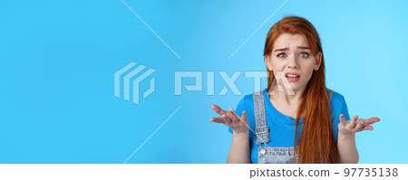 Puzzled confused redhead cute woman look ambushed, raise hands shrugging uncertain, frowning perplexed, cannot understand what happened, stand frustrated upset blue background Puzzled confused redhead cute woman look ambushed, raise hands shrugging uncertain, frowning perplexed, cannot understand what happened, stand frustrated upset blue background 97735138