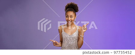 Good-looking excited glamour african-american female student attend luxurious event in silver shiny perfect dress dancing look around pointing right left smiling pleased variants make choice 97735452