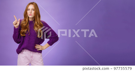 I am watching you. Portrait of bossy and suspicious cute redhead sister in purple sweater squinting doubtful and serious as making assumptions or hesitating pointing at upper left corner I am watching you. Portrait of bossy and suspicious cute redhead sister in purple sweater squinting doubtful and serious as making assumptions or hesitating pointing at upper left corner 97735579
