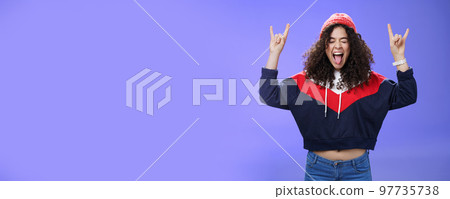 Waist-up shot of rebellious and carefree woman having fun feeling excited and awesome at party close eyes sticking out tongue and showing rock-n-roll signs, wearing beanie and warm clothes Waist-up shot of rebellious and carefree woman having fun feeling excited and awesome at party close eyes sticking out tongue and showing rock-n-roll signs, wearing beanie and warm clothes 97735738